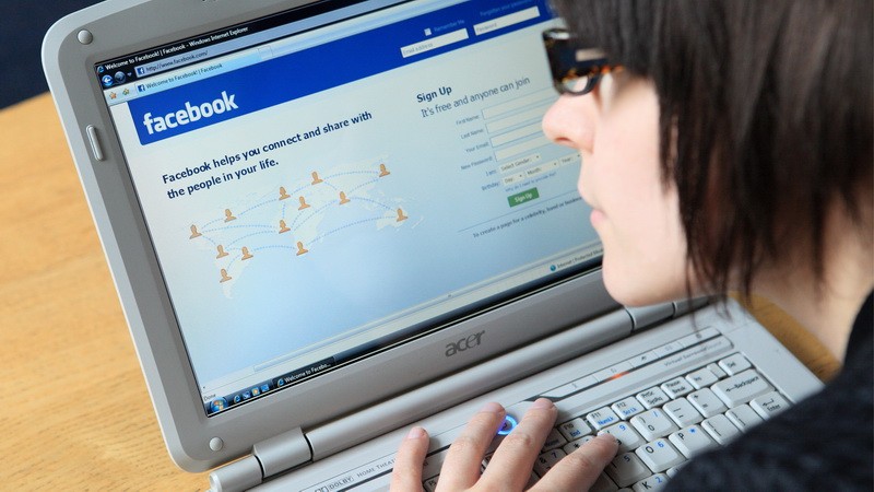 Žena za počítačom, facebook v pozadí